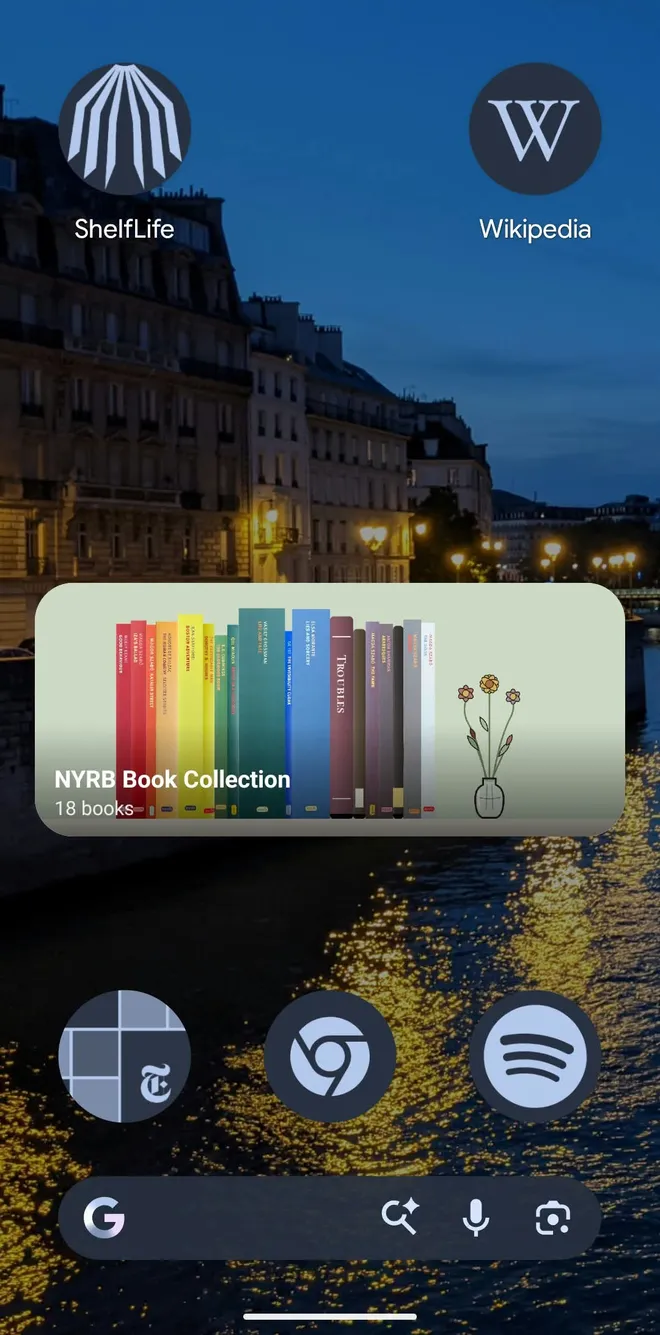 Android home screen with a wide ShelfLife widget showing a shelf named NYRB Book Collection, 18 books, in rainbow spine order on a sage backdrop beside a vase of flowers